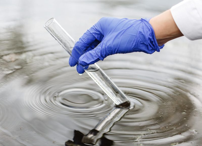 Researcher holds a test tube with water in a hand in blue glove